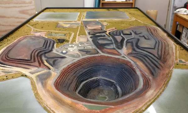 Scale architectural model of an open-pit mine with terraced layers and facility structures on display for project presentation.