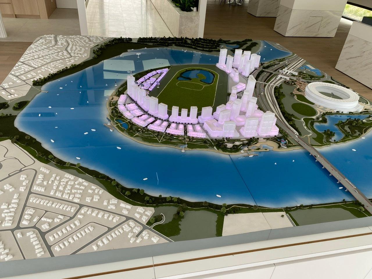 Architectural scale model of a waterfront city featuring illuminated buildings, green spaces, and water elements.