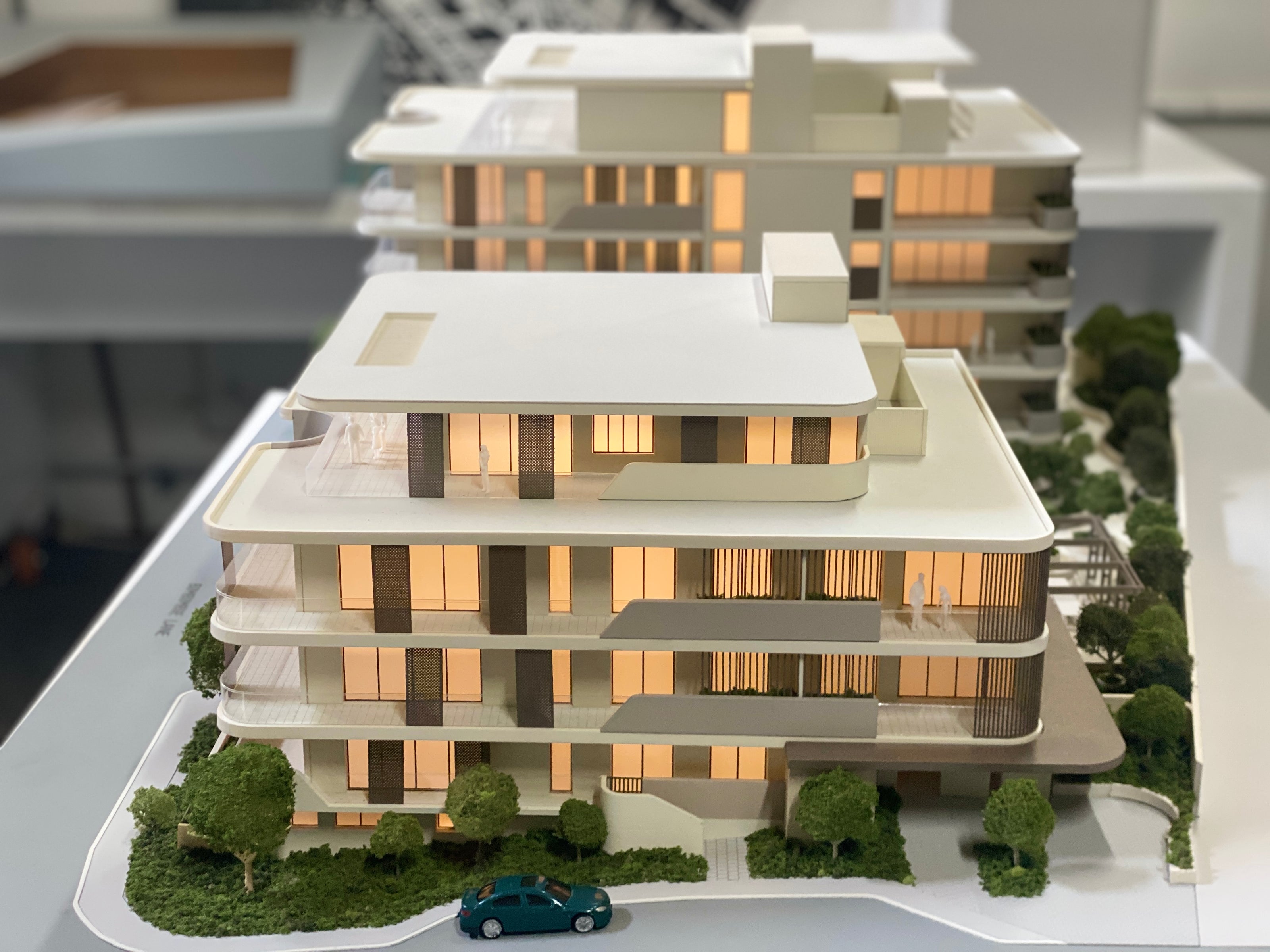 Architectural scale model of a modern multi-story building featuring illuminated windows and landscaped greenery.