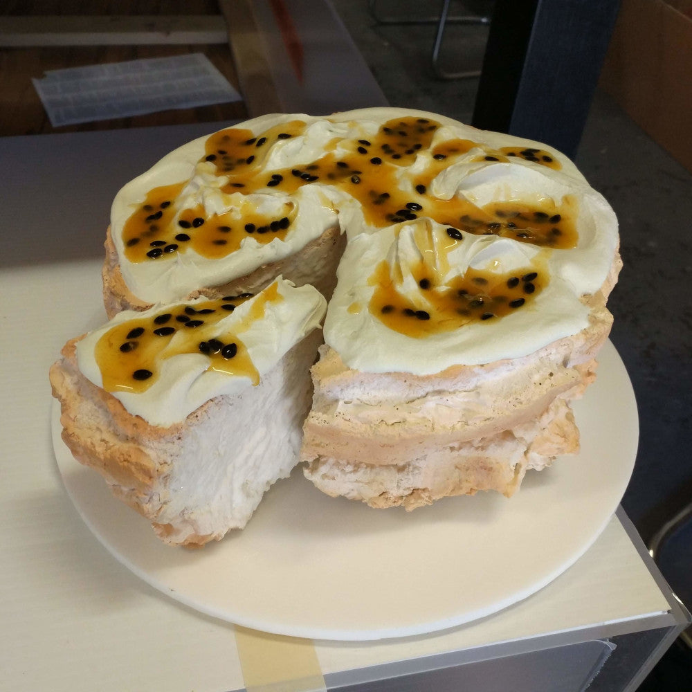 Pavlova cake with whipped cream and passionfruit on white plate, resembling an apartment display model with a slice missing.