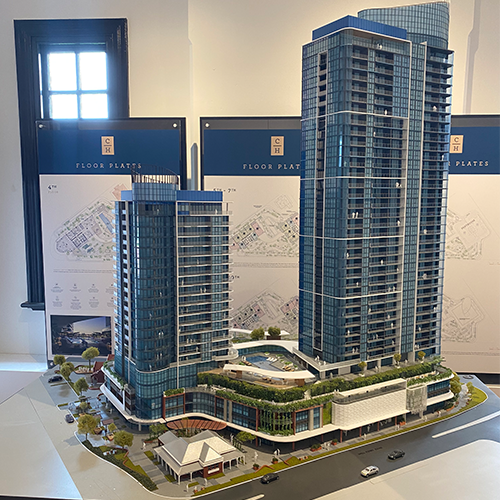 Architectural scale model of two modern high-rise buildings with landscaped grounds and floor plan displays in sales gallery.