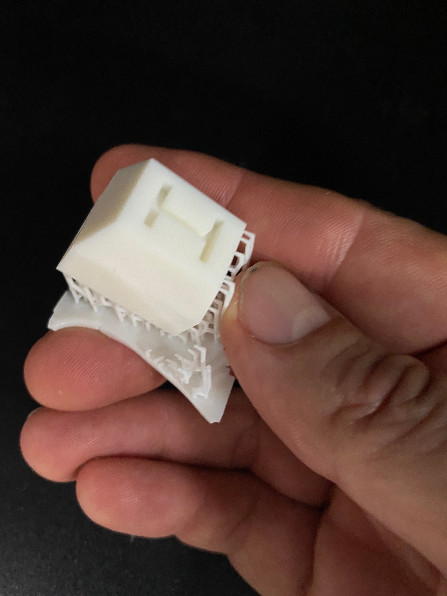 Hand holding an architectural scale model of a white house with detached roof, black background, home design display.