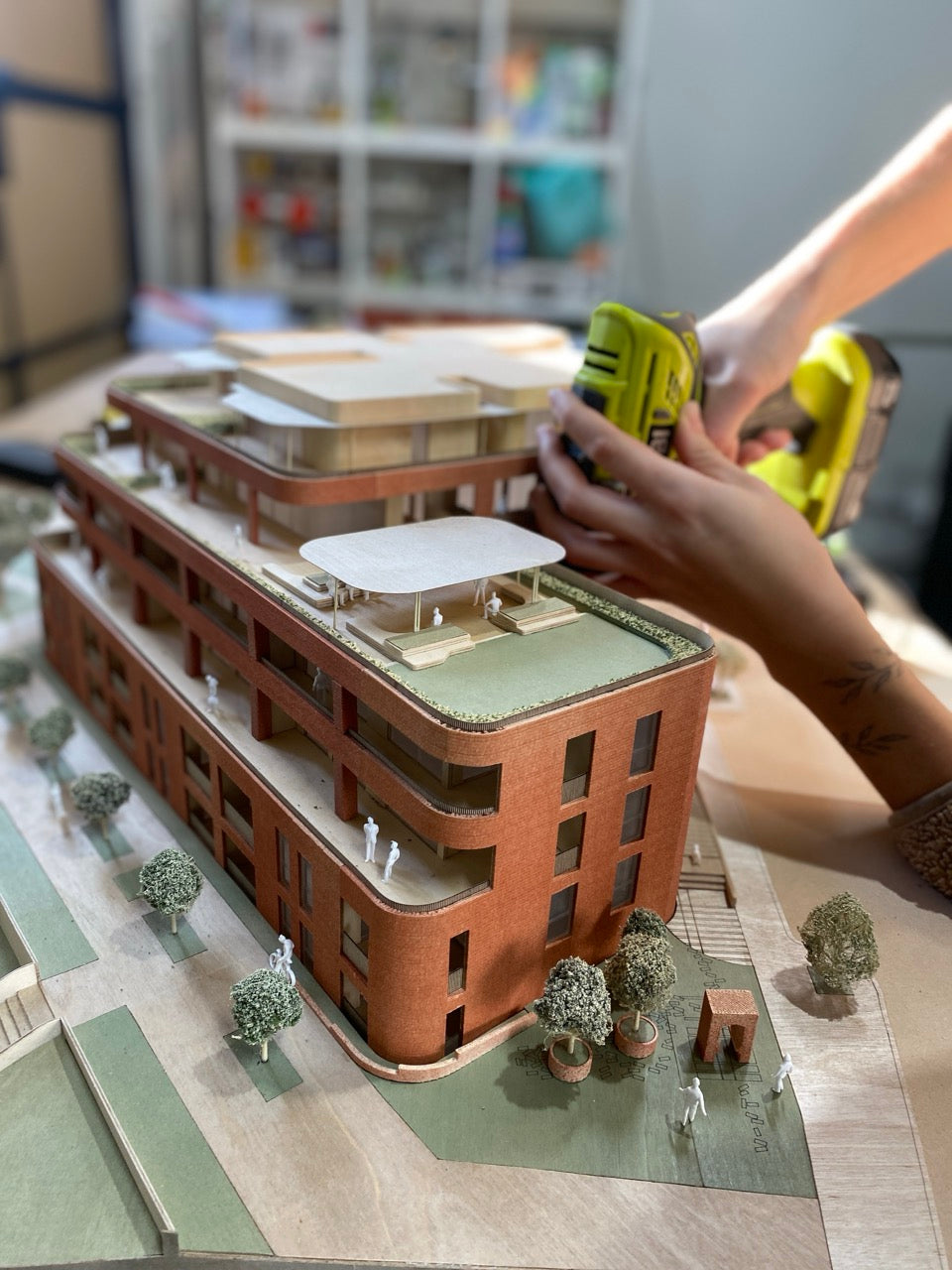 Hands use a power tool on a modern architectural scale model of a multi-story apartment building.